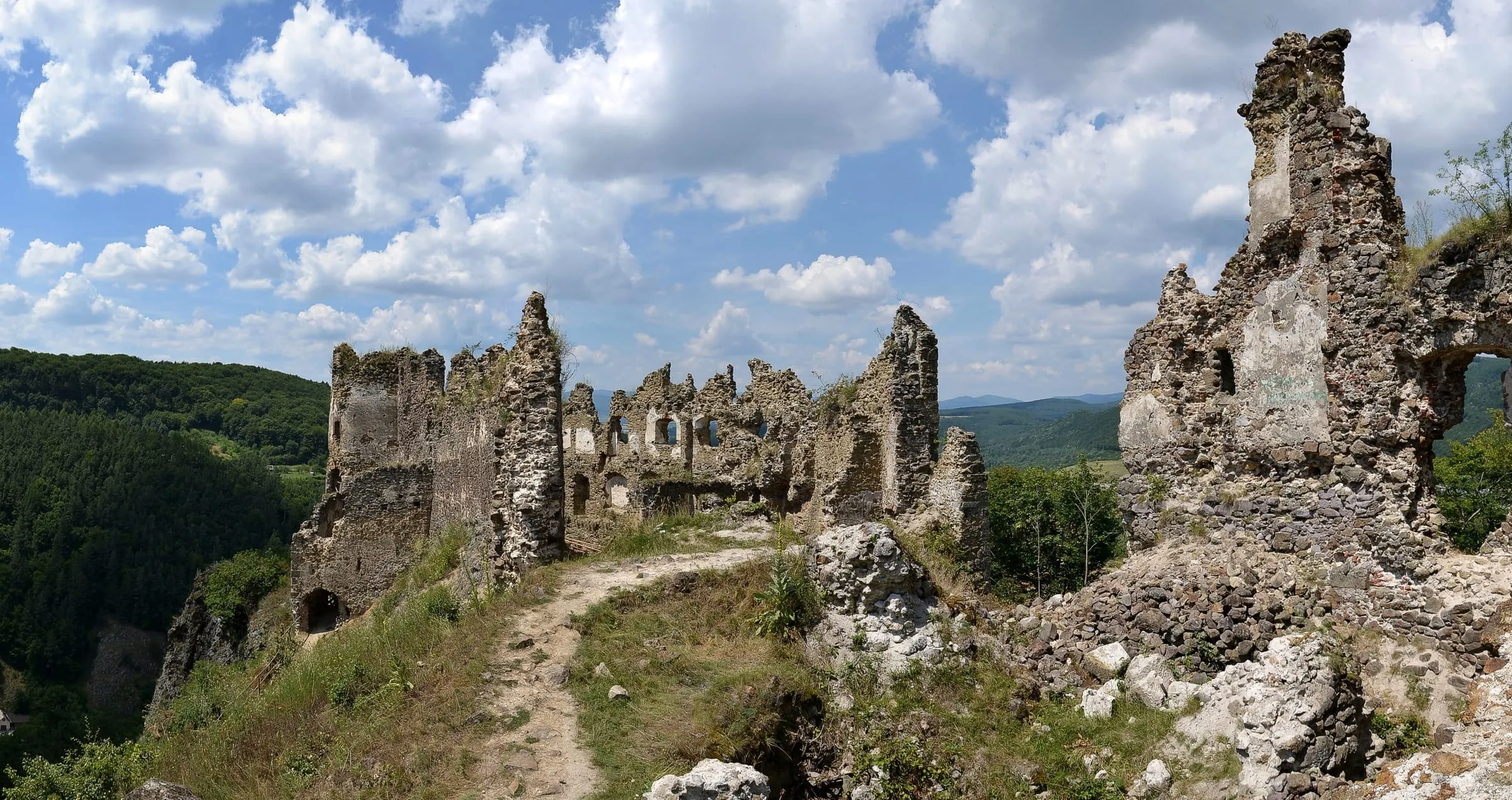 Pěšina vede do zříceniny hradu Šášov na Slovensku, v létě pod kupovitými mraky.